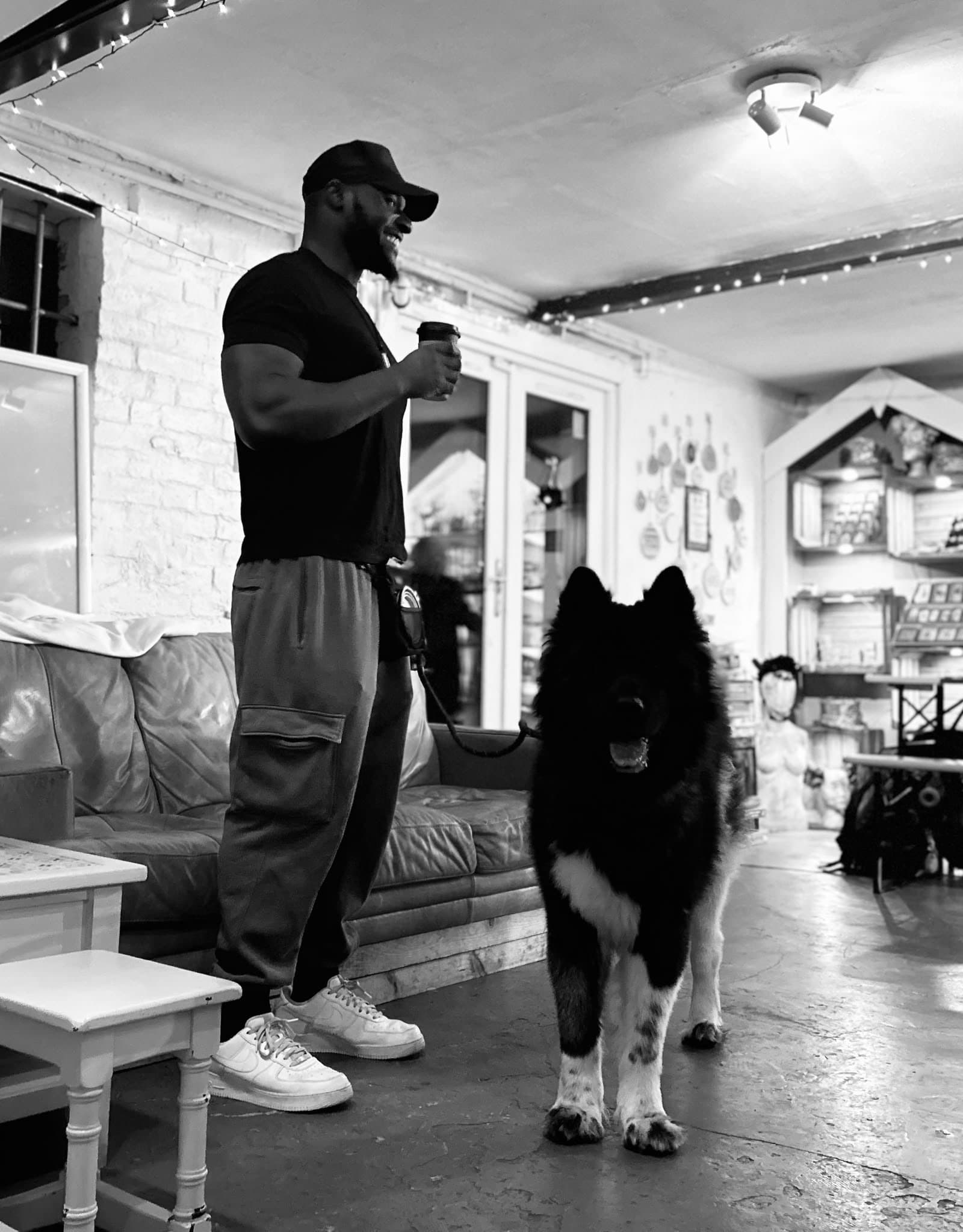 Dami smiling with a coffee in a cafe, Atlas standing beside him on a loose lead