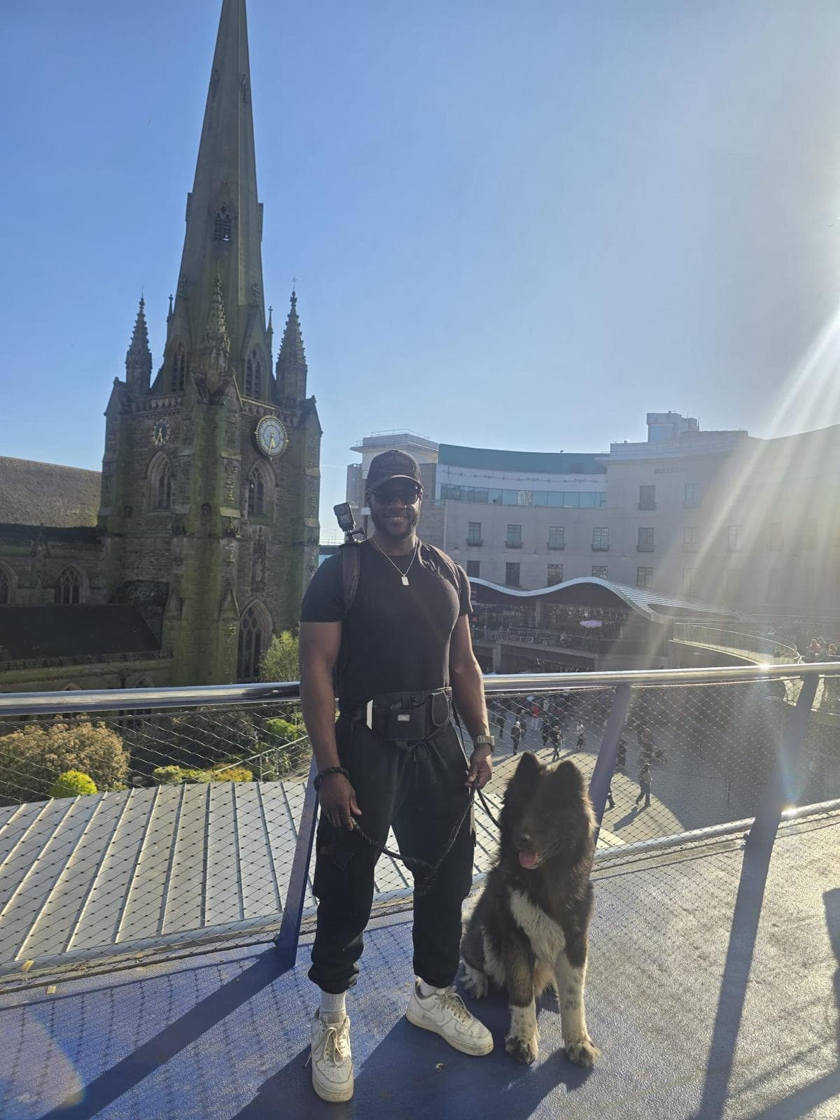Dami smiling beside Atlas, who is sitting on a lead on a city walkway
